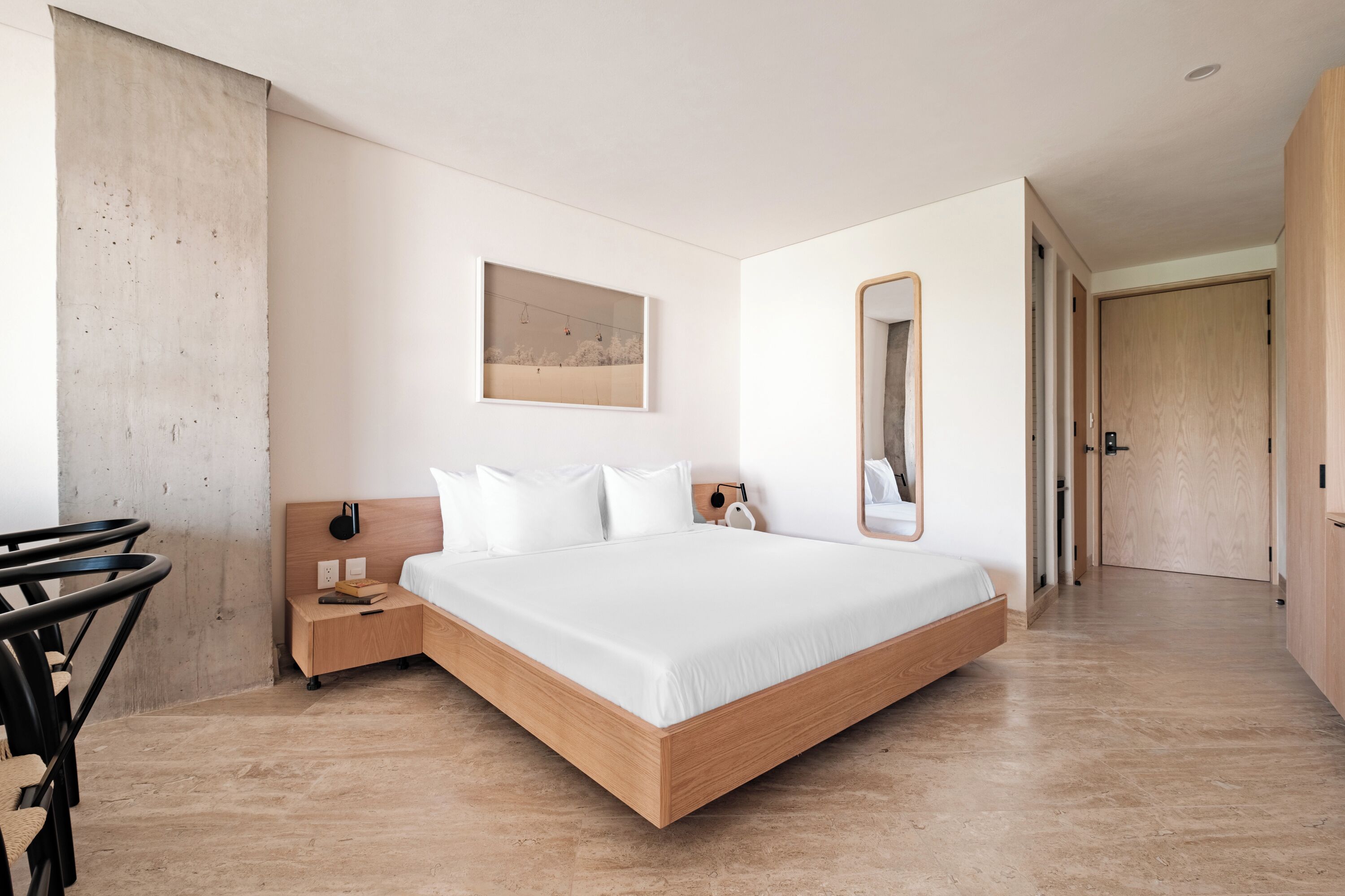 A modern bedroom with a large bed, a bedside table, a nightstand, a mirror, and a wall-mounted artwork.