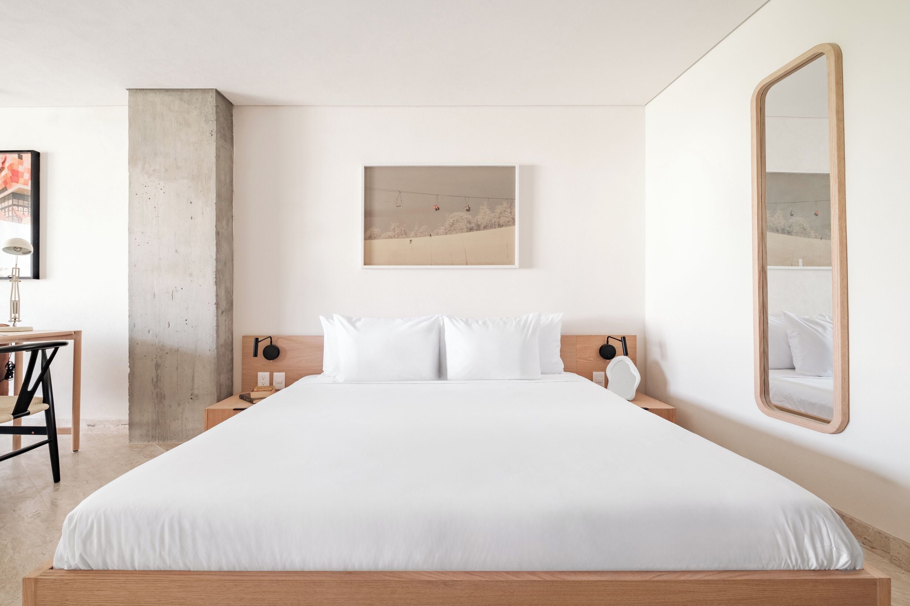 A modern bedroom with a large bed, a wooden headboard, a nightstand, a bedside table, a framed picture on the wall, and a mirror.