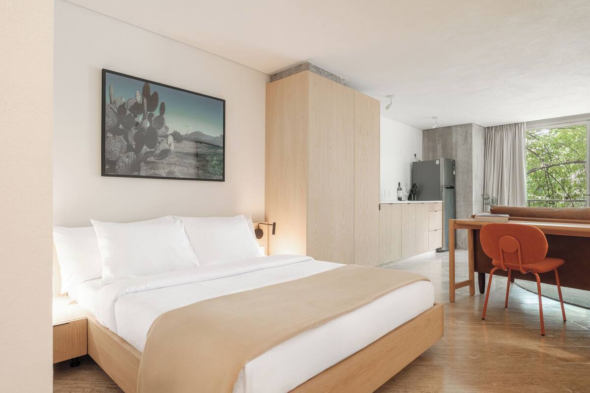 A modern hotel room with a bed, a desk, and a kitchenette.