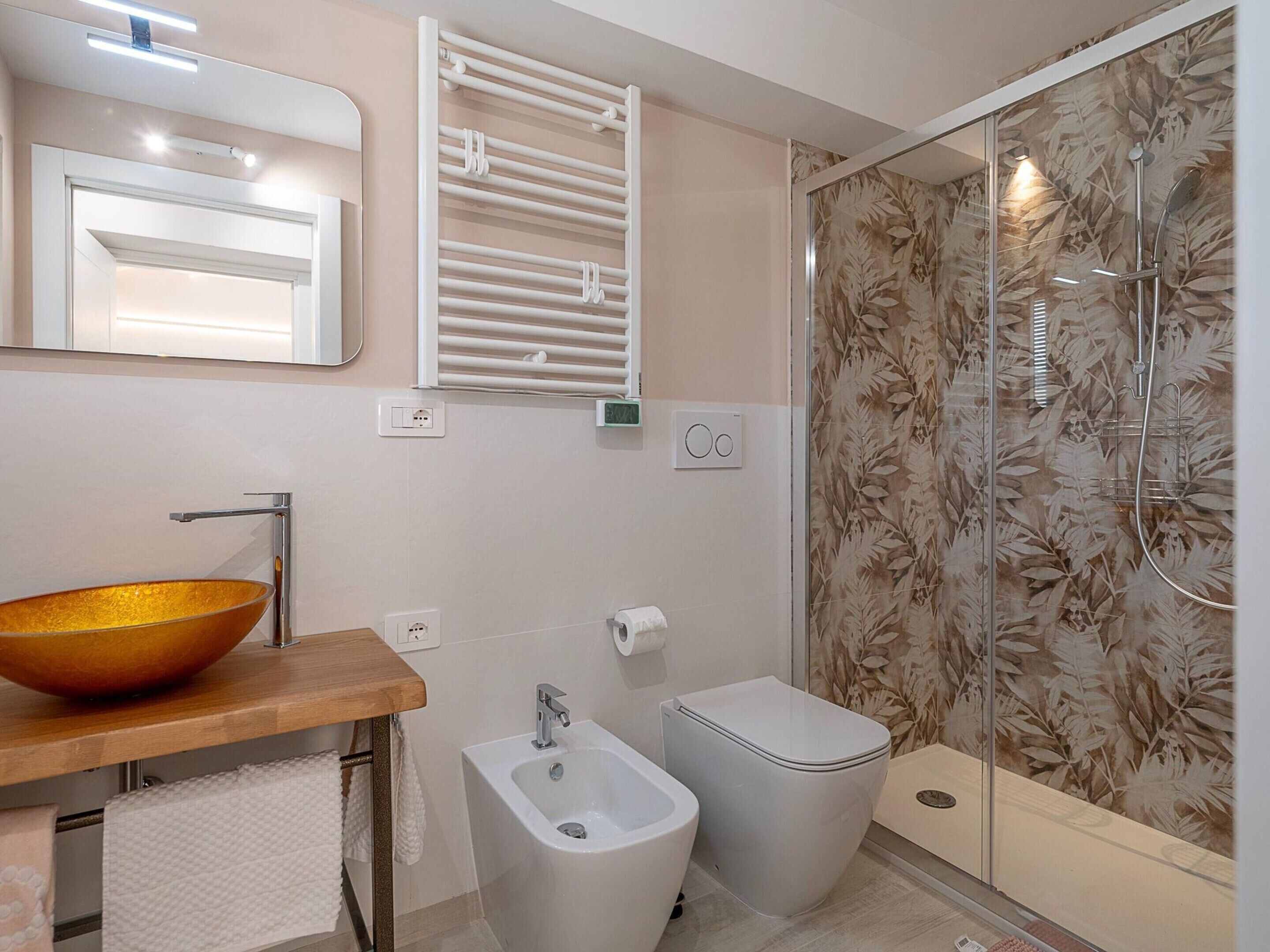 A modern bathroom with a glass shower, a wooden vanity with a bowl sink, a bidet, and a toilet.