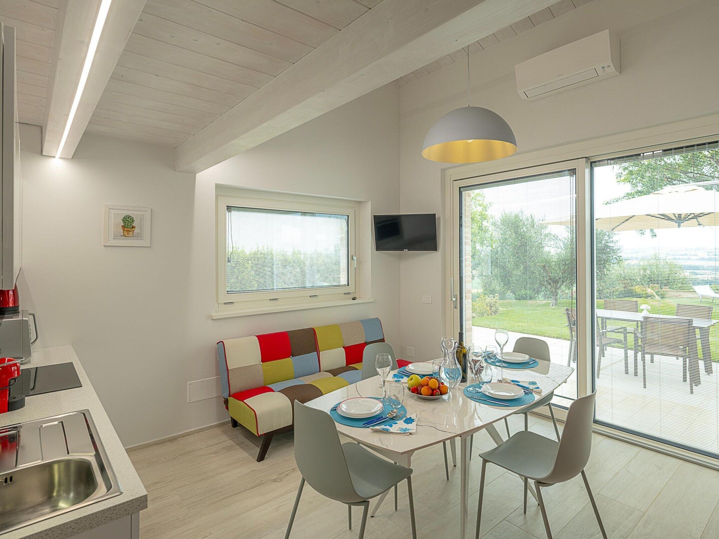 A modern kitchen with a built-in oven, a dining area with a white table set for four, and a colorful bench.