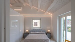 Ein modernes Schlafzimmer mit einem großen Bett, zwei Nachttischen, einem Fenster und Blick ins Freie.