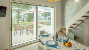 Ein moderner Essbereich mit einer großen Schiebetür, die auf eine Terrasse führt, einem Tisch gedeckt mit blauen Untersetzern und Tellern sowie einer Treppe mit Metallgeländer.