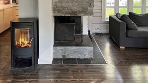 A modern living room with a stone fireplace, a built-in stove, and a dark wooden floor.