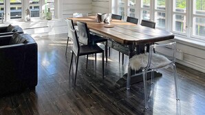 A dining area with a wooden table and chairs, large windows, and a dark wooden floor.