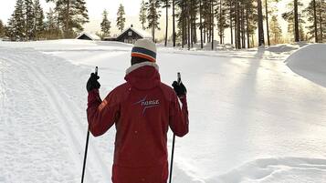 A person in a red jacket with 'Norge' on the back, standing in a snowy area with trees and a cabin in the background.