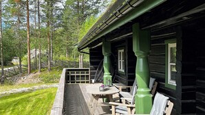 A wooden deck with outdoor seating, a window, and a view of a forested area.