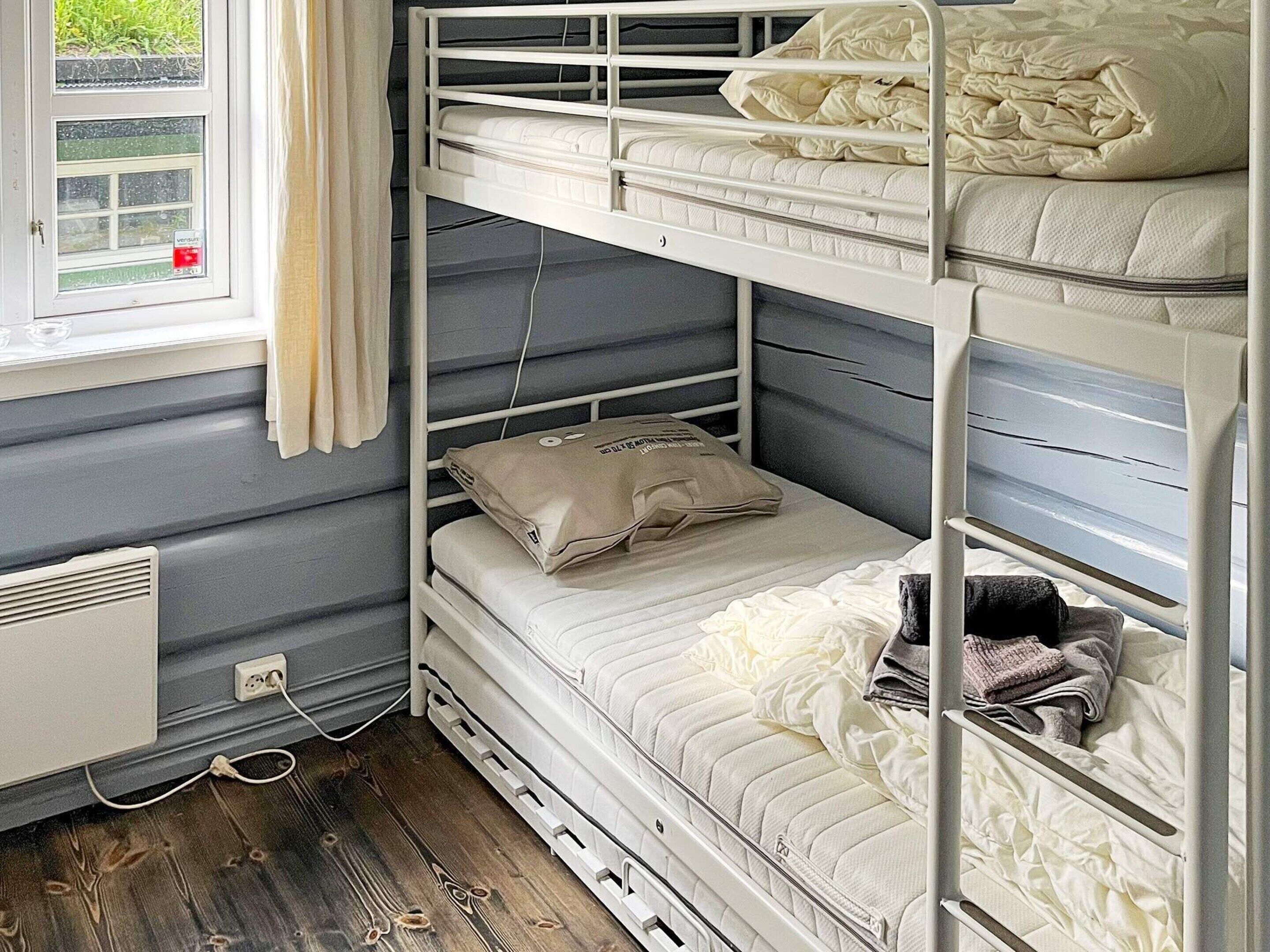 Een slaapkamer met een stapelbed, een raam, een radiator en een stopcontact.