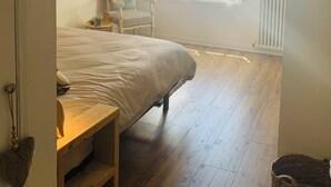 A bedroom with a large bed, a chair, a small table, and a window with blinds. - Ground floor flat with garden - 3*** furnished holiday home- all comforts - wifi (Saintes)