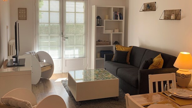 A modern living room with a sofa, coffee table, and a dining area with a table set for two. - Ground floor flat with garden - 3*** furnished holiday home- all comforts - wifi (Saintes)