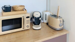 A kitchen with a microwave, coffee maker, toaster, and a shelf with a plant and a framed picture. - Ground floor flat with garden - 3*** furnished holiday home- all comforts - wifi (Saintes)