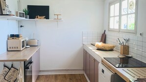 A modern kitchen with wooden flooring, white cabinets, a microwave, a toaster, and a sink. - Ground floor flat with garden - 3*** furnished holiday home- all comforts - wifi (Saintes)