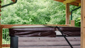 Una terraza de madera con un jacuzzi, un banco y vistas a vegetación exuberante.