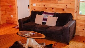 Interior acogedor de una cabaña con techo de madera, un candelabro, un sofá, una mesa de centro y una puerta.