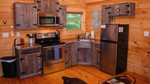 Cocina rústica de cabaña de madera con microondas, horno y refrigerador integrados.
