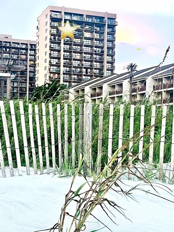 Een hoog gebouw met meerdere balkons, een houten hek en wat groen op de voorgrond.