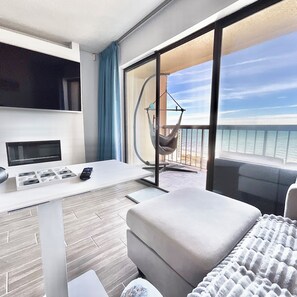 Een moderne hotelkamer met balkon, een sofa, een tafeltje met telefoon en een televisie.