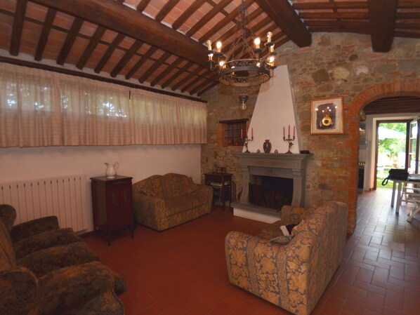 A cozy living room with a fireplace, patterned sofas, and a stone wall. - Cottage in San Gennaro With Private Pool (Lucca)