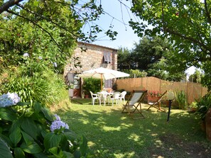 A garden patio with a table and chairs, surrounded by lush greenery and a stone building in the background. - Cottage in San Gennaro With Private Pool (Lucca)