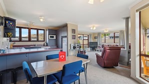 Een moderne keuken met een centraal eiland, een eetgedeelte met blauwe stoelen, en een gezellige woonkamer met een open haard.