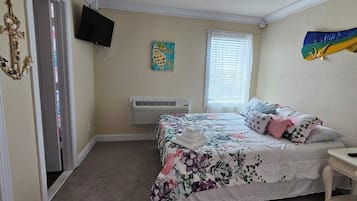 Une chambre à coucher avec un lit, une table de chevet avec une lampe, un téléviseur fixé au mur, une fenêtre avec des stores et un poisson décoratif accroché au mur.