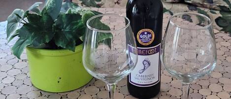 A bottle of wine, two empty wine glasses, and a potted plant on a tiled floor.