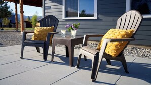 Two Adirondack chairs with yellow cushions on a patio with a table and a vase of flowers.
