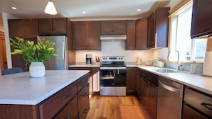 A modern kitchen with wooden cabinets, stainless steel appliances, and a central island with a potted plant.