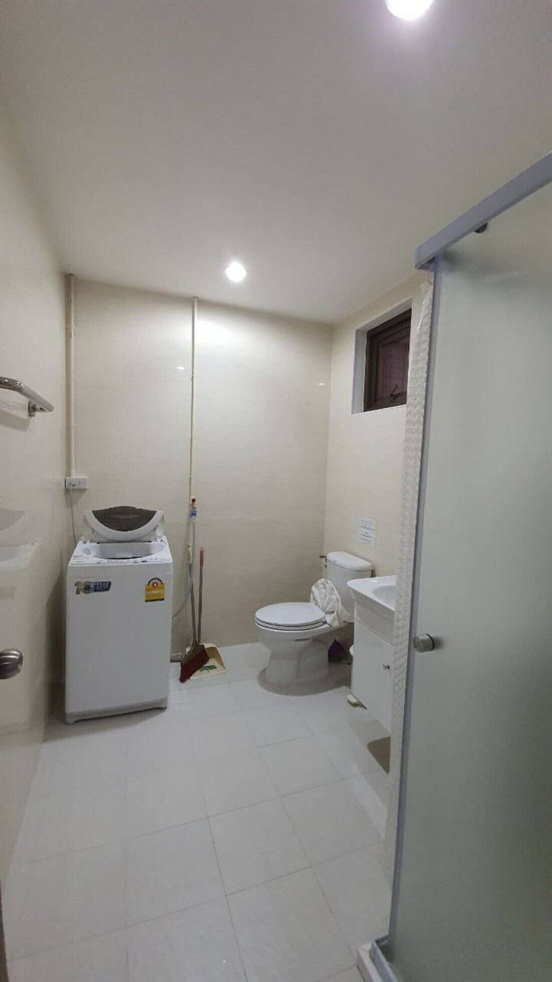A small, compact bathroom with a toilet, a washing machine, and a shower area.