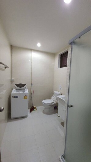 A small, compact bathroom with a toilet, a washing machine, and a shower area.