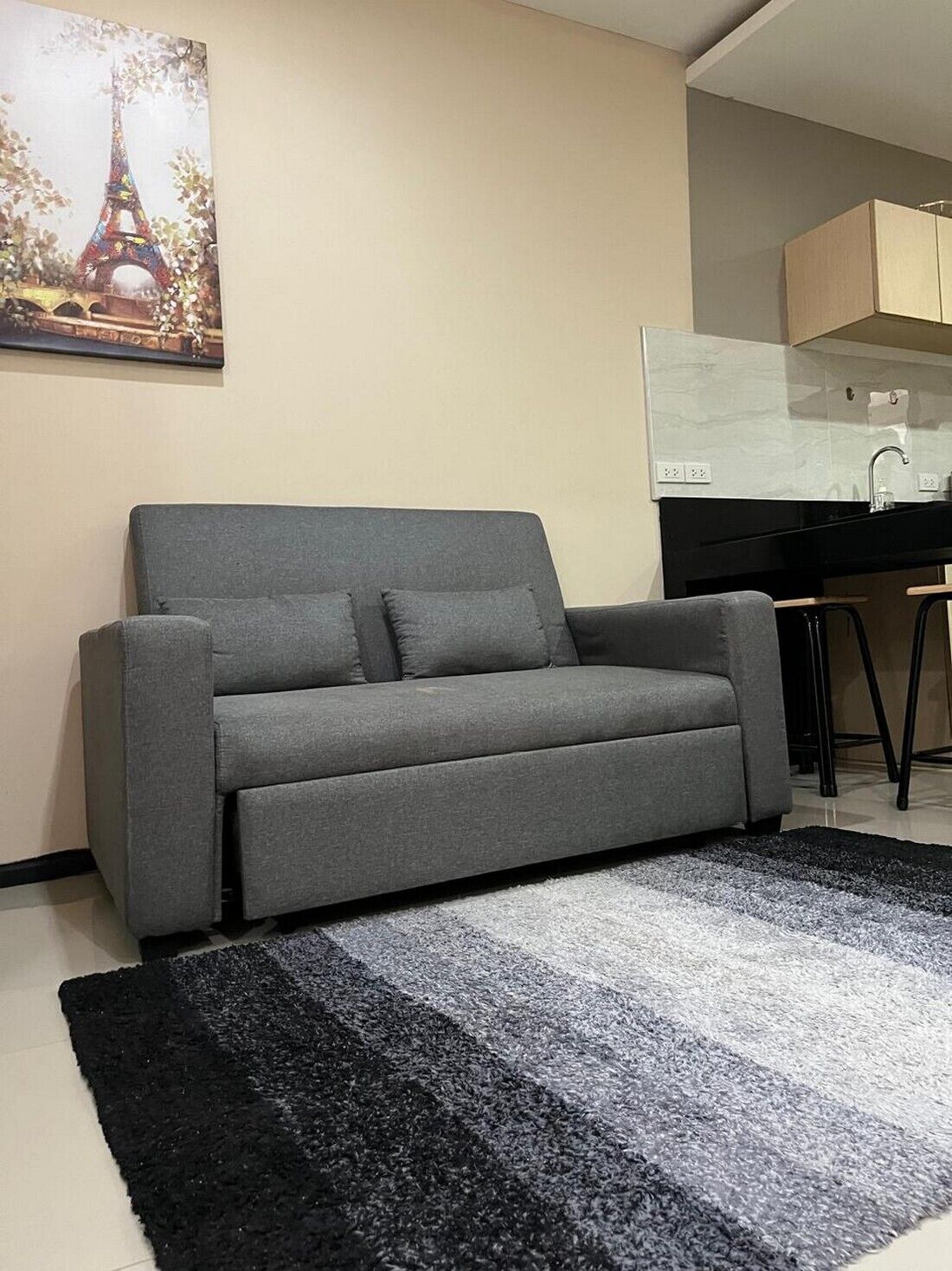 A grey sofa with a black and grey rug in a modern living area with a kitchen in the background.