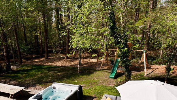 An outdoor patio with a hot tub, seating area, and a swing set in a wooded area. - Spacious Retreat, Vlagtwedde (Vlagtwedde)