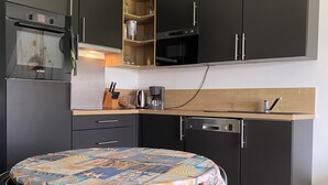 A modern kitchen with dark cabinetry, a Bosch oven, a coffee maker, and a round table with chairs. - Ty Houat, Petit Coin de Paradis (Ile de Houat)