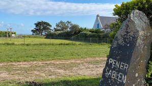 A stone marker with inscriptions, a grassy field, a building in the background, and a clear sky. - Ty Houat, Petit Coin de Paradis (Ile de Houat)