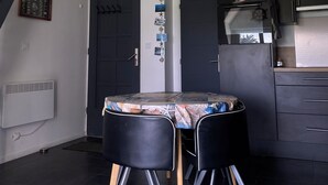 A modern kitchen with dark cabinets, a built-in oven, and a dining area with two black chairs and a table. - Ty Houat, Petit Coin de Paradis (Ile de Houat)