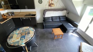 A modern living space with a kitchen, a black leather sofa, a round table, and a view of the outdoors. - Ty Houat, Petit Coin de Paradis (Ile de Houat)