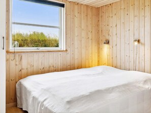 A room with wooden panel walls, a large window with a view of greenery, and a bed with a white bedspread. - Luxury Retreat by Beach - By Traum Ferienwohnungen (Idestrup)