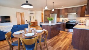 A modern kitchen with wooden cabinets, a central island, and a dining area with a blue sofa and wooden chairs.
