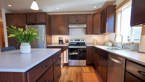 A modern kitchen with wooden cabinets, stainless steel appliances, and a central island with a potted plant.