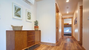 A hallway with wooden flooring, a wooden cabinet with a basket, two framed leaf artworks, and a potted plant.