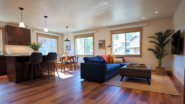 A modern living room with a blue sofa, wooden flooring, and large windows.