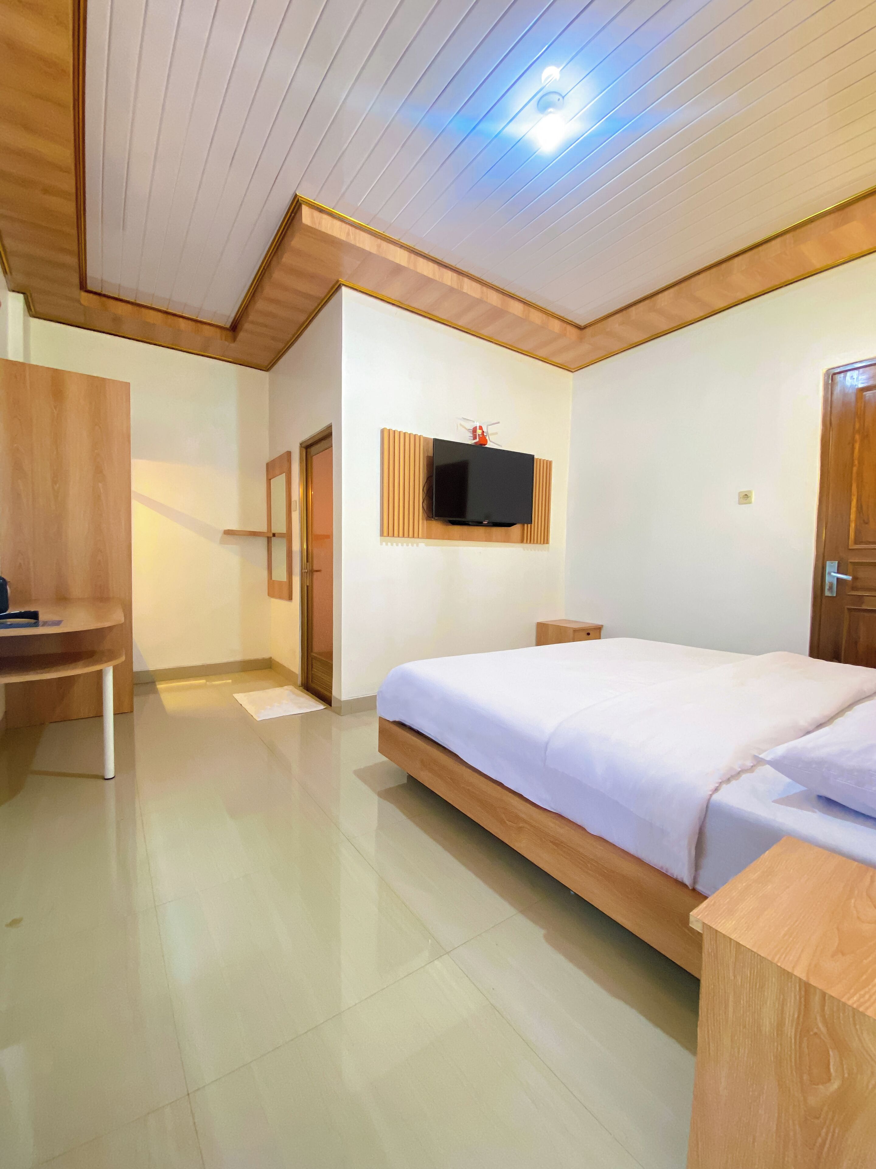 Un dormitorio con cama, televisión montada en la pared y escritorio de madera.