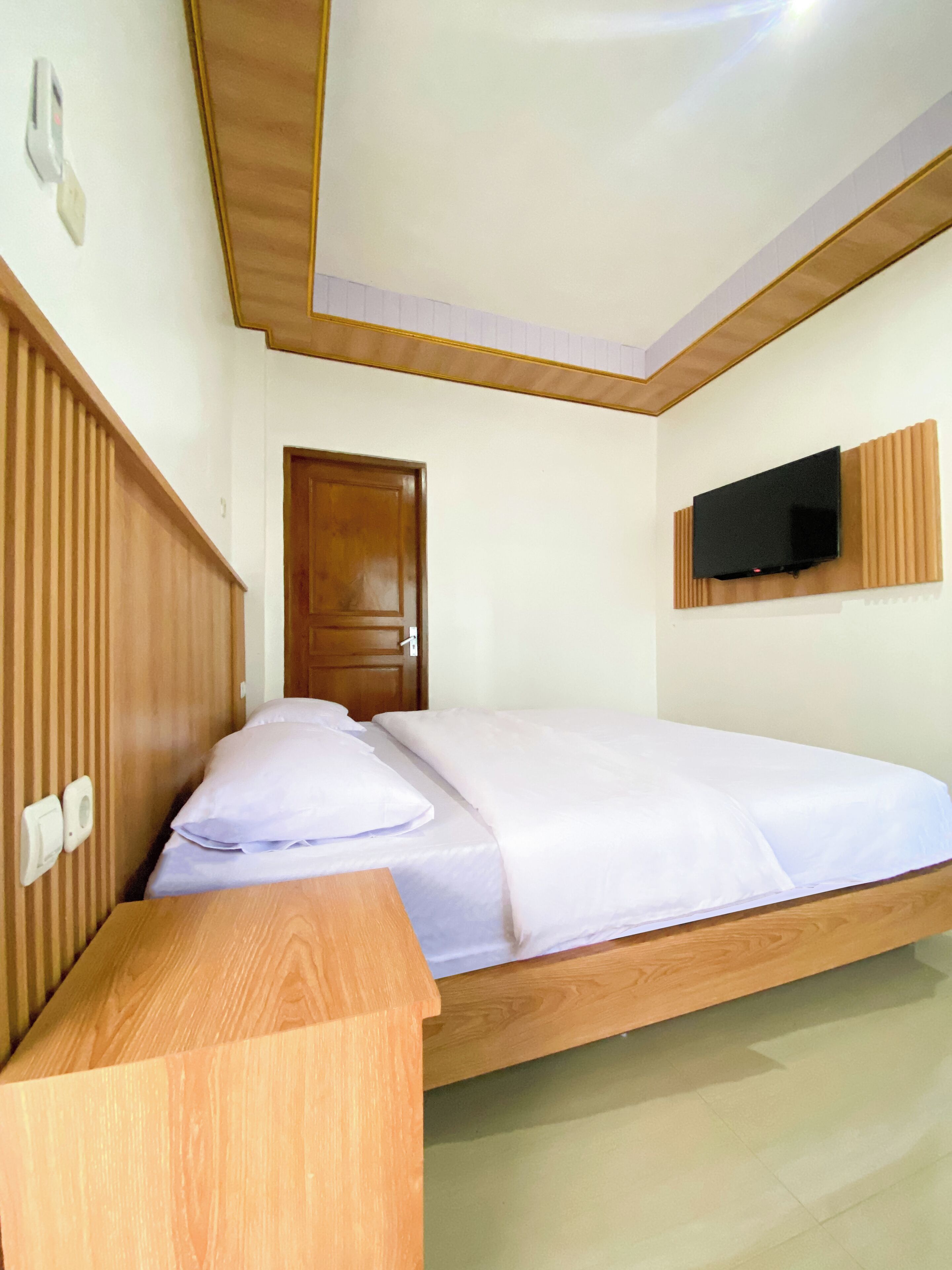 A bedroom with a wooden bed, a television mounted on the wall, and a wooden wardrobe.