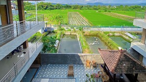 A view from a balcony overlooking a swimming pool, a garden, and agricultural fields.