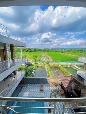 Vista desde un balcón sobre una piscina, un jardín y campos de cultivo.