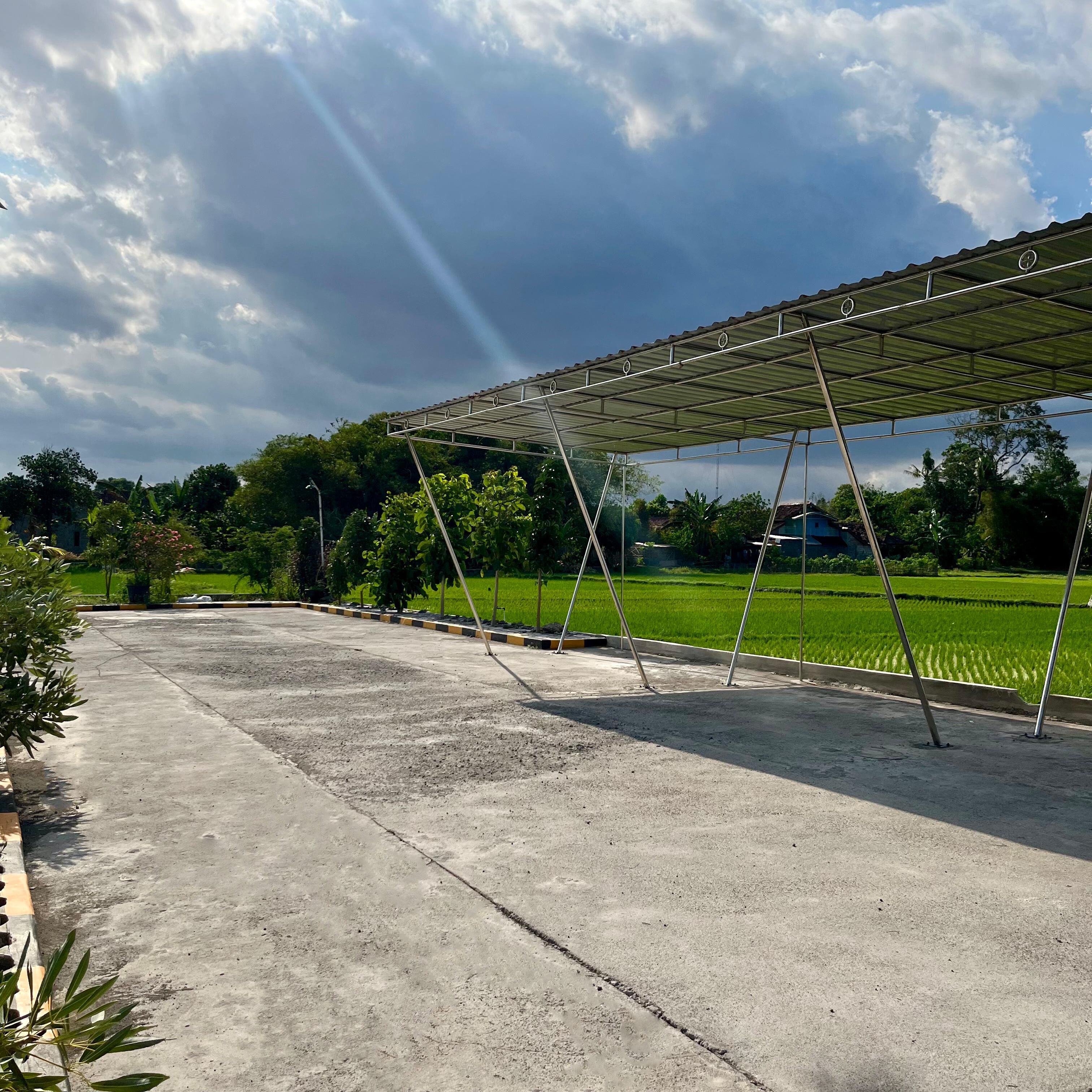 Un espace extérieur abrité, doté d’un sol en béton, entouré de verdure et avec un champ en arrière-plan.