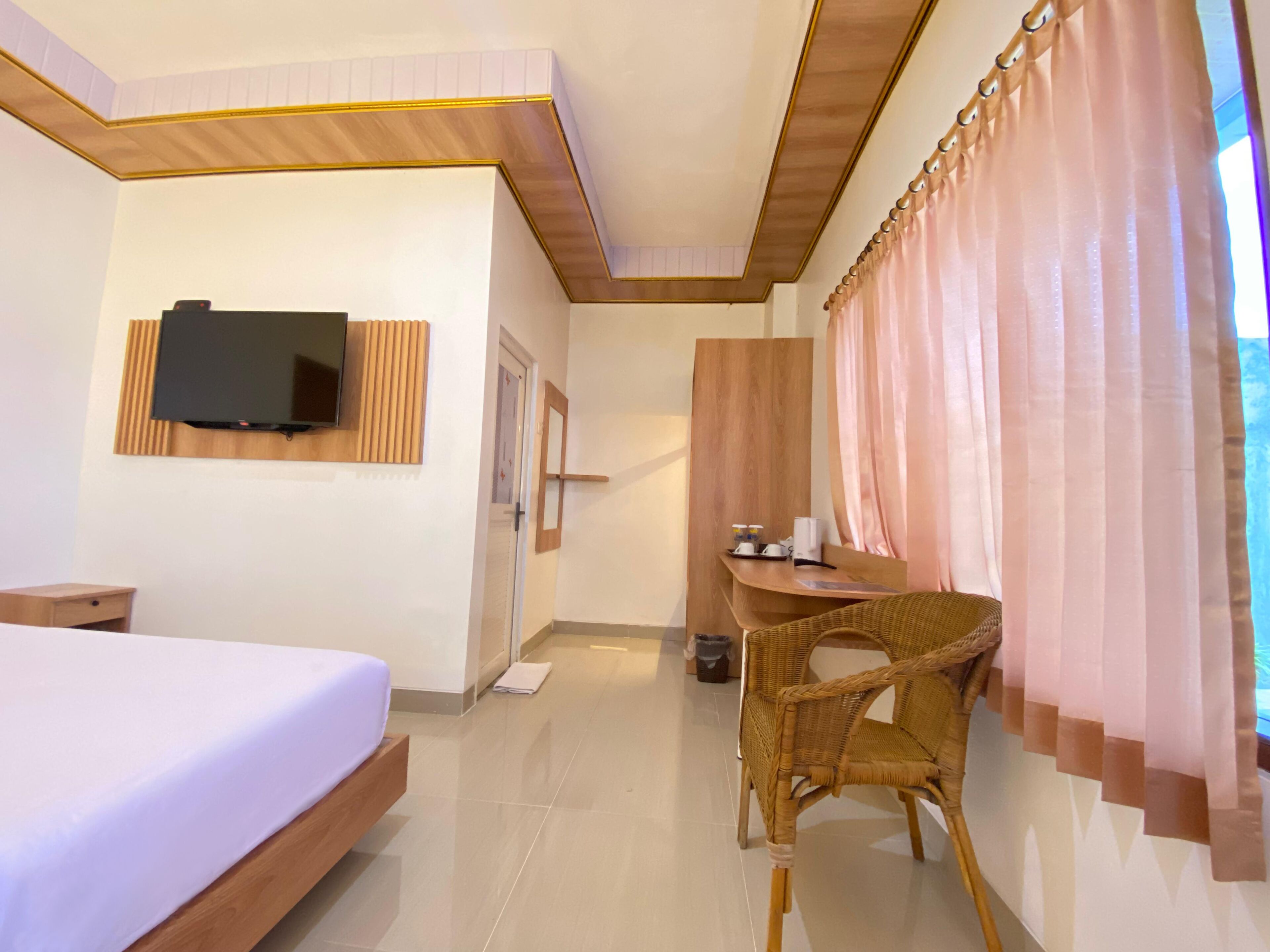 A hotel room with a bed, a TV mounted on the wall, a desk with a chair, and a window with curtains.