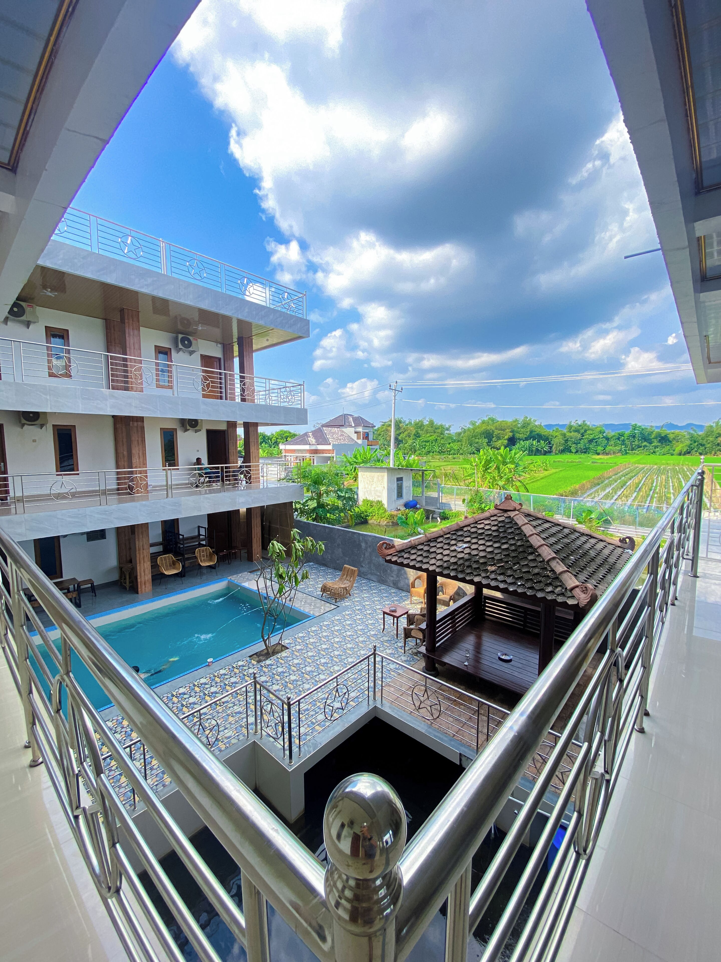 A multi-story hotel with a rooftop pool, outdoor seating, and a view of a green landscape.