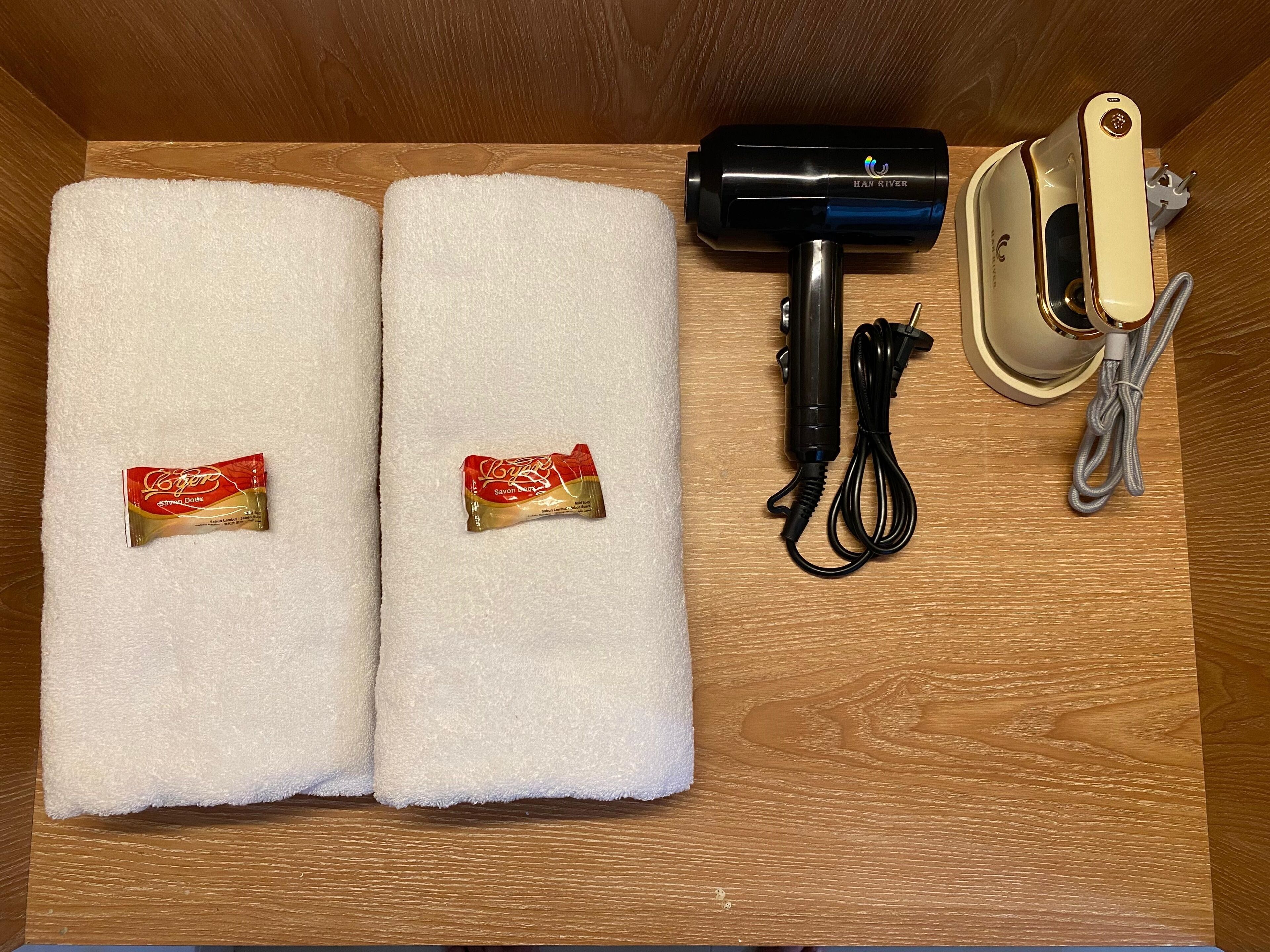 A wooden drawer containing a hair dryer, a plug, and two tubes of hand sanitizer.