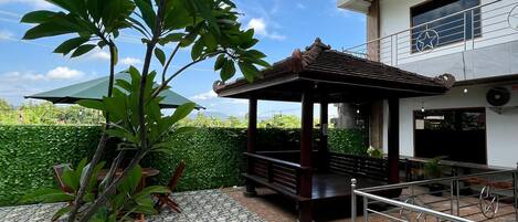 A patio area with a tiled floor, a wooden gazebo, and a large tree.